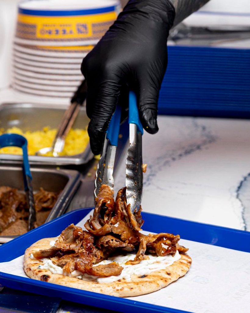 Spit-roasted gyro meat being piled onto warm pita